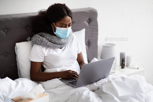 Sick black woman in face mask surfing on Internet