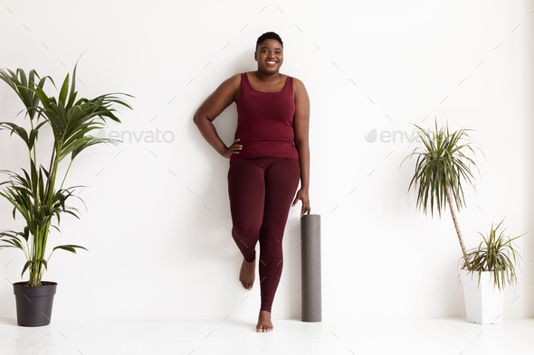Joyful chubby black lady standing by wall with fitness mat Stock Photo by  Prostock-studio