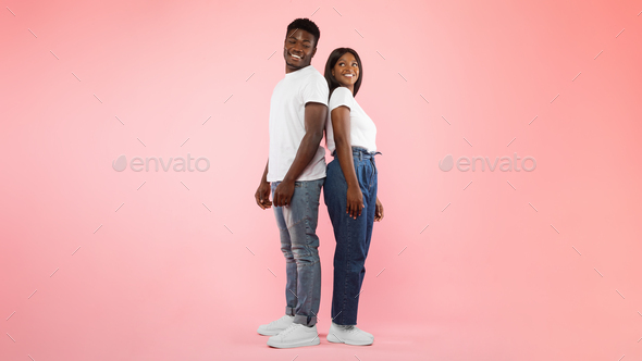 Confident couple standing back to back at pink studio background