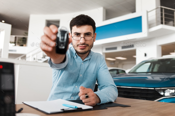Auto salesman shows a car key while sitting at a table in a auto showroom