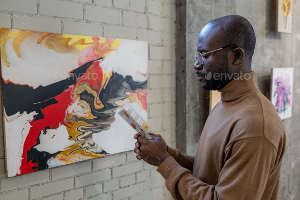 Serious African man with leaflet standing in front of painting