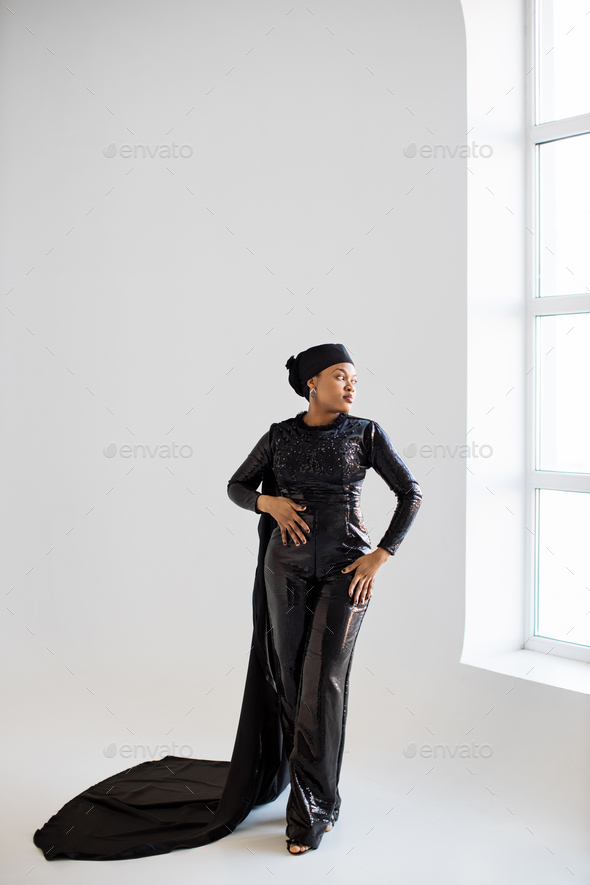 African woman in hijab and black evening wear posing indoors