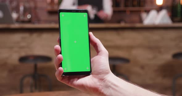 Man Holds a Modern Smartphone with Green Screen on alt