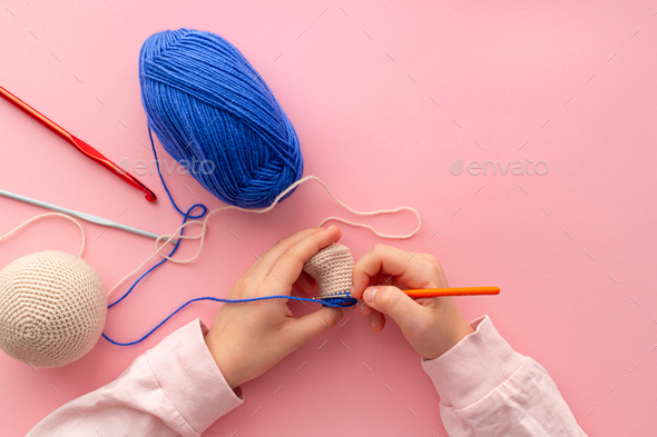 Children\'s hands in the process of crocheting toys from blue and beige yarn.
