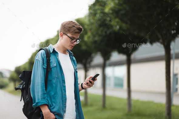 Young handsome guy student uses smartphone to access internet. Gadget addiction concept