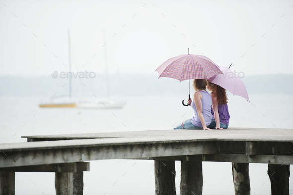 Germany, Bavaria, Ammersee, Two Women sitting on jetty, holding umbrella, rear view