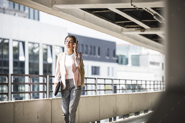Young businesswoman walking in parking garage, listeing music with her headphones