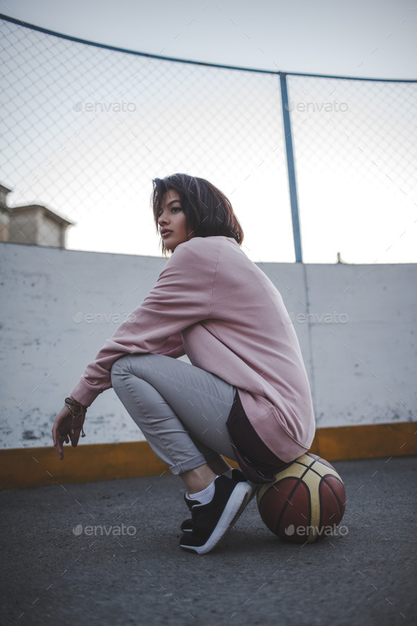 Young woman sitting on basketball outdoors