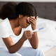 Upset african american woman sitting on bed with pregnancy test - PhotoDune Item for Sale