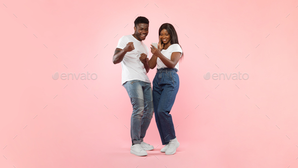 Black couple using phone celebrating success shaking fists