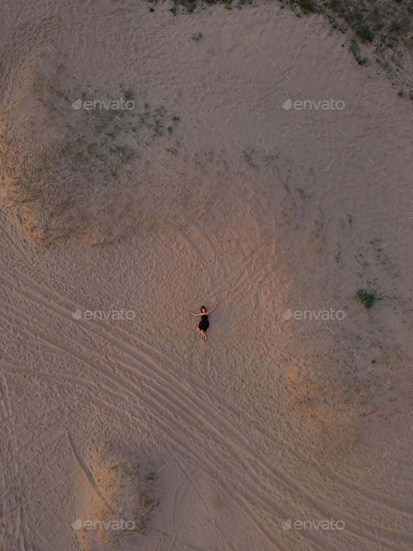 Young woman in a black dress lying on the back on the sand. Top view from the drone.