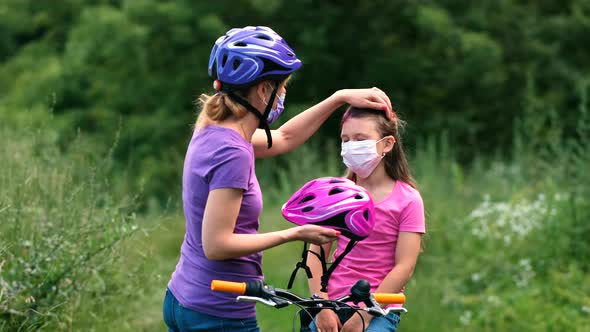 Mother attaching her daughters cycling helmet. They are wearing medical masks