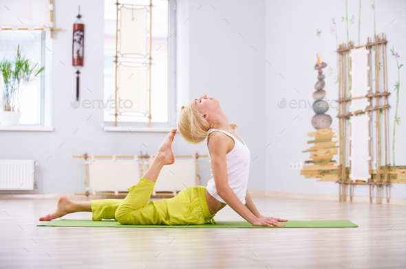 Beautiful sporty fit yogi woman practices yoga lying asana Ardha Bhujangasana in the fitness room