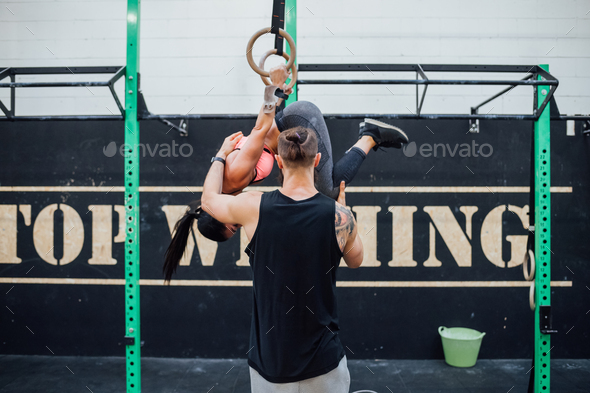 Young woman training with rings helped by her personal trainer