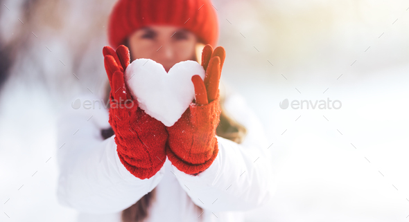 Woman in red gloves and hat holding heart shape from snow