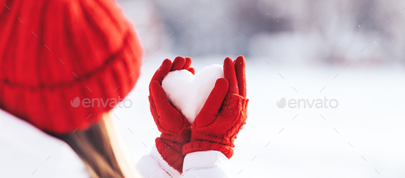 Woman in red gloves and hat holding heart shape from snow
