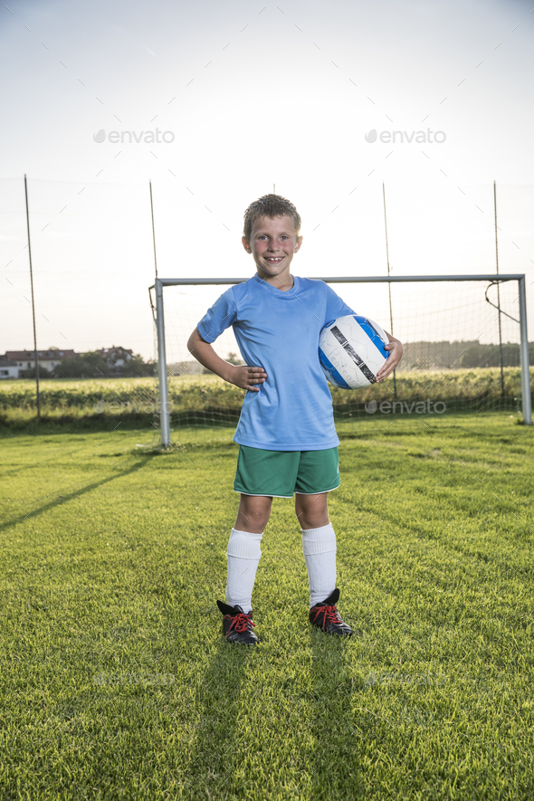 Portrait of smiling young football player holding ball on football ground