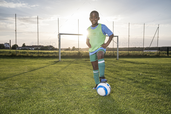 Portrait of confident young football player with ball on football ground