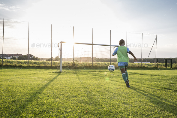 Young football player on football ground at sunset