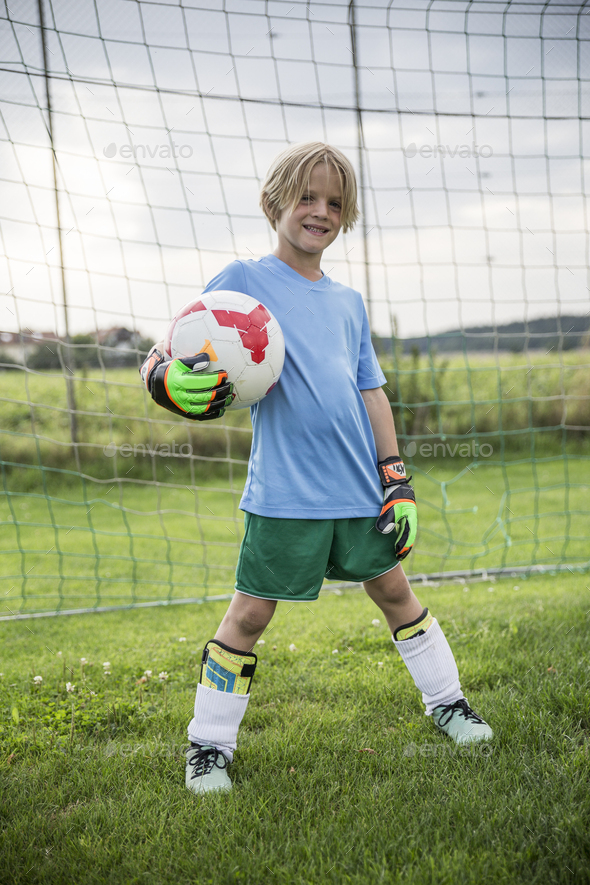 Portrait of smiling young football goalkeeper holding ball on football ground