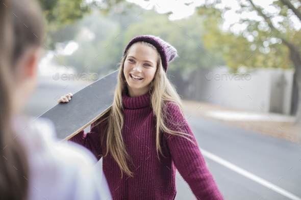 Smiling teenage girl holding skateboard meeting with friend