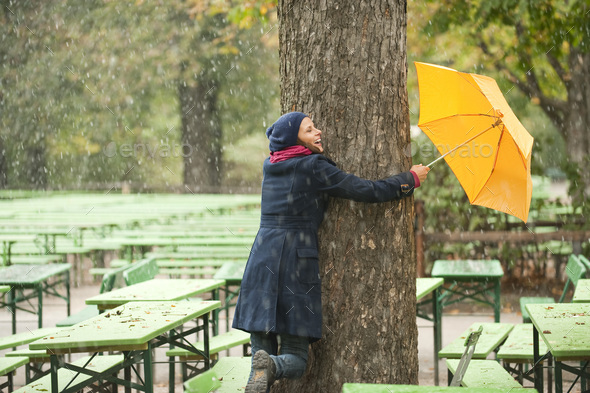 Germany, Bavaria, Munich, English Garden, Woman in beer garden embracing tree, holding umbrella, lau