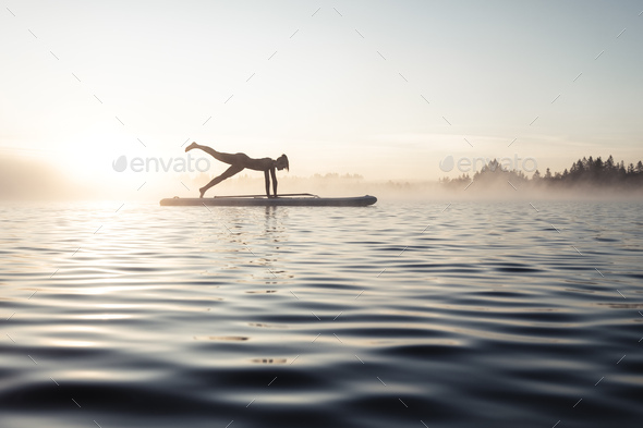 Woman practicing paddle board yoga on lake Kirchsee in the morning, Bad Toelz, Bavaria, Germany