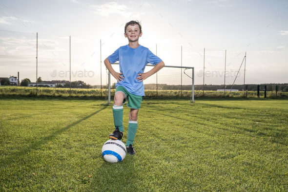 Portrait of confident young football player with ball on football ground