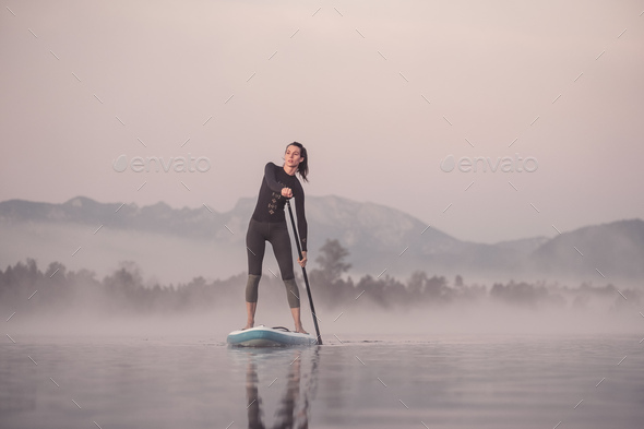 Woman stand up paddling on lake Kirchsee at morning mist, Bad Toelz, Bavaria, Germany