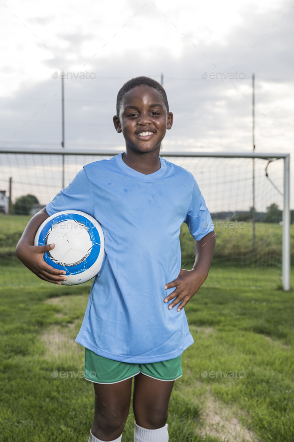Portrait of smiling young football player holding ball on football ground