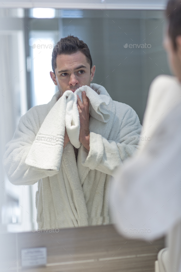 Mirror image of man watching himself while drying his face with towel