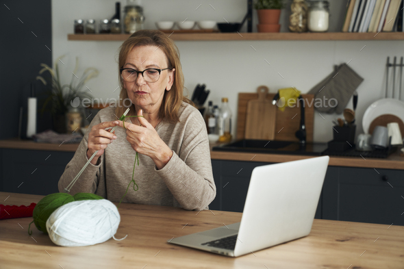 Senior caucasian woman at home learning how to knit from video tutorial