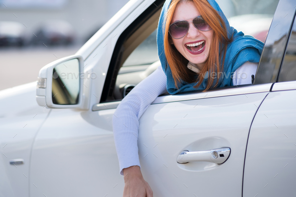 Young fashionable smiling woman driver looking out the window behind car steering wheel - Stock Photo - Images