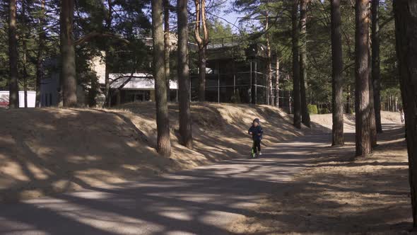 Happy Cute Little Boy Riding an Kick Scooter in the Park at Sunny Spring Day alt