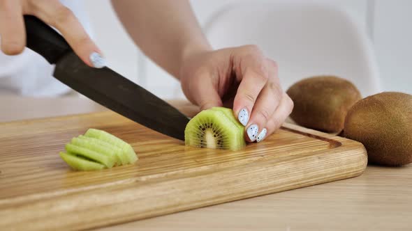 Woman Cut the Kiwi on a Wooden Board in the Kitchen alt
