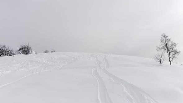 Aerial View of Snowy Mountain Peak with Ski Tracks on Snow in a Winter and Foggy Journey