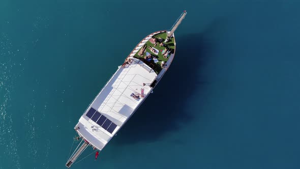Top View of a Large Yacht in the Blue Waters of the Sea and Tourists Having a Rest on the Deck alt