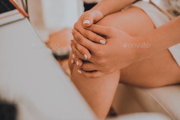 The girl sits with her legs crossed at a white cosmetic table