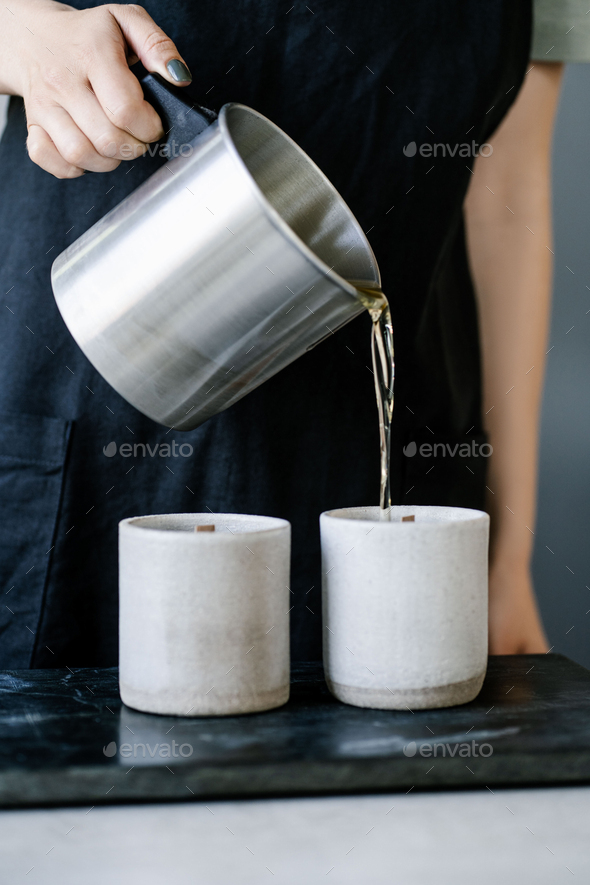 The girl pours wax into a gray concrete candle mold.