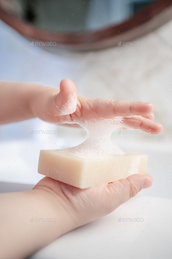 The child holds the soap and covers the foam with the second hand