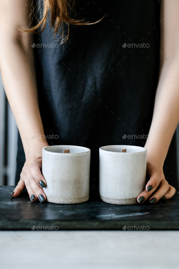 The girl pours wax into a gray concrete candle mold.