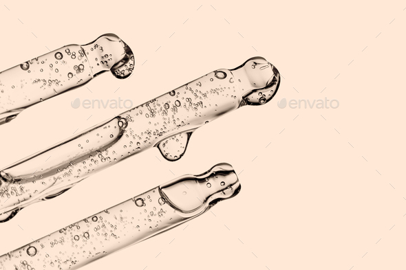 Three transparent pipettes with cosmetics on a beige background.