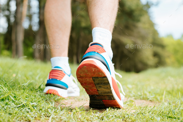 Hiking on summer day, outdoors. Man walking in nature, close-up of red sports sneakers. Dirty boot