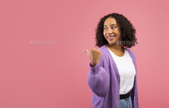Happy young black woman pointing aside at free space on pink studio background