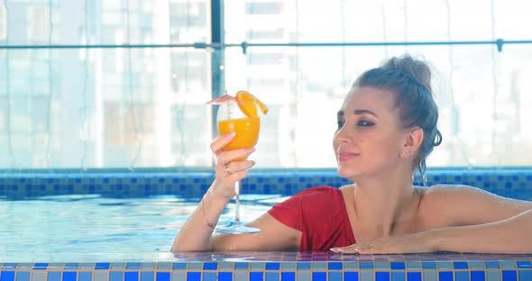 Lady Tastes Orange Cocktail with Umbrella Decoration in Pool
