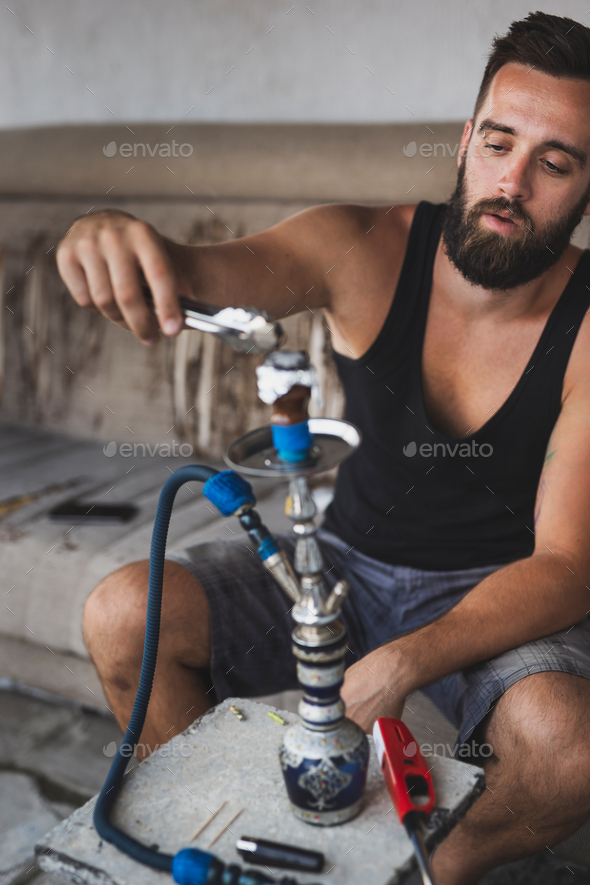 Man placing charcoal on hookah tobacco