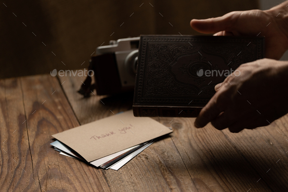 Man holding an old book in front of a wooden table with a retro camera and postcards
