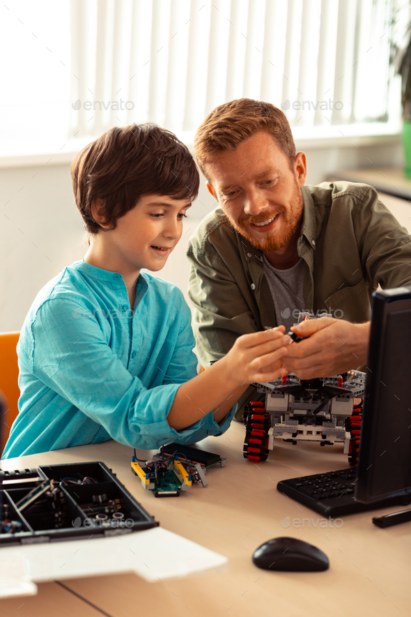 Science teacher helping his pupil with robot building