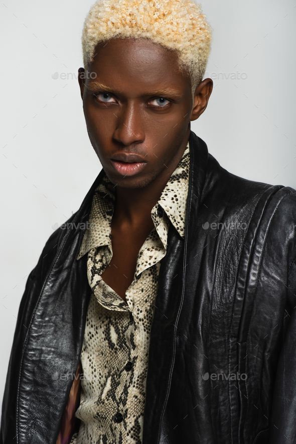 blonde african american man in leather jacket and snakeskin print shirt isolated on grey