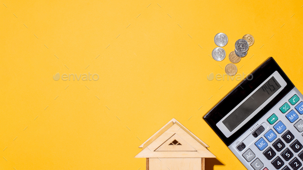 Coins, calculator and toy house, top view. Yellow background, copy space. Concept of rent payment